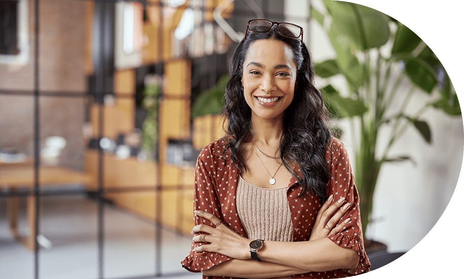 Mulher de pele morena sorrindo, ela utiliza camisa morrom com bolinhas brncas, e está de braços cruzados.